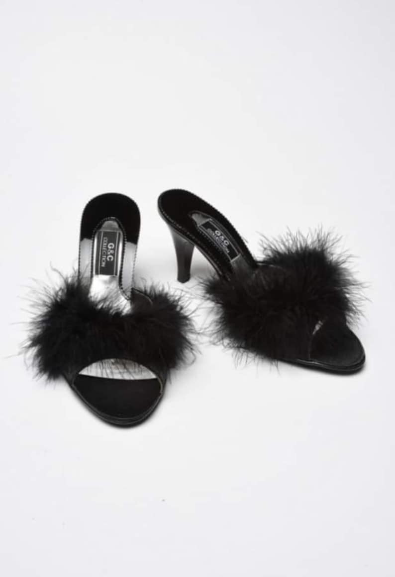 May include: Pair of black satin heeled slippers with black feather trim. The slippers have a pointed toe and a high heel. The brand name "G&C Collection" is printed on the side of the slippers.