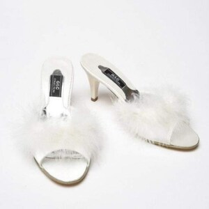 May include: White satin heeled slippers with fluffy white feather trim. The slippers have a black label that reads "G&C Collection".