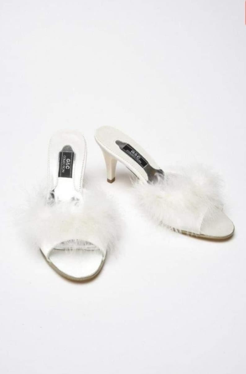 May include: White satin heeled slippers with fluffy white feather trim. The slippers have a black label that reads "G&C Collection".