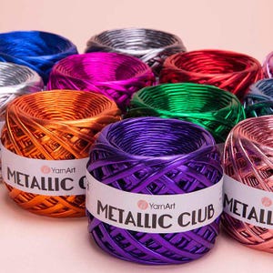 Può includere: Assortimento di filati metallici in vari colori, tra cui argento, rosso, rosa, arancio, verde, viola e oro. Il filato è avvolto in gomitoli ed etichettato "YarnArt Metallic Club".
