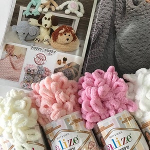 May include: Three skeins of Alize Puffy yarn in white, pink, and light pink. The yarn is soft and fluffy, and is perfect for crocheting or knitting. The yarn is packaged in clear plastic bags with the Alize Puffy logo and the words "Soft & Quick" printed on them.