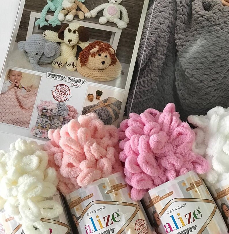 May include: Three skeins of Alize Puffy yarn in white, pink, and light pink. The yarn is soft and fluffy, and is perfect for crocheting or knitting. The yarn is packaged in clear plastic bags with the Alize Puffy logo and the words "Soft & Quick" printed on them.