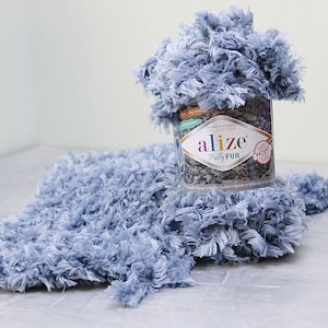 Könnte beinhalten: Eine Spule hellblaues Alize Puffy Fur Garn. Das Garn befindet sich in einem durchsichtigen Plastikbehälter mit einem Etikett, auf dem "Alize Puffy Fur" und "No Needles No Hooks Collection" steht.