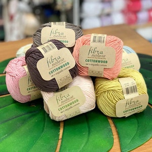 May include: Six balls of organic cotton yarn in various colors, including pink, brown, beige, and yellow. Each ball has a label that reads "fibra natura COTTONWOOD 100% organic cotton".