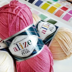 Pode incluir: Dois novelos de fio, um rosa e um creme, com a etiqueta "alize Diva Plus Silky & Mercerized Effect" no novelo rosa.