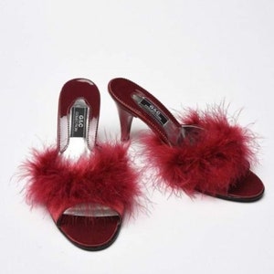 May include: A pair of red satin heeled slippers with fluffy feather trim. The slippers have a clear heel and the brand name "G&C Collection" is printed on the insole.