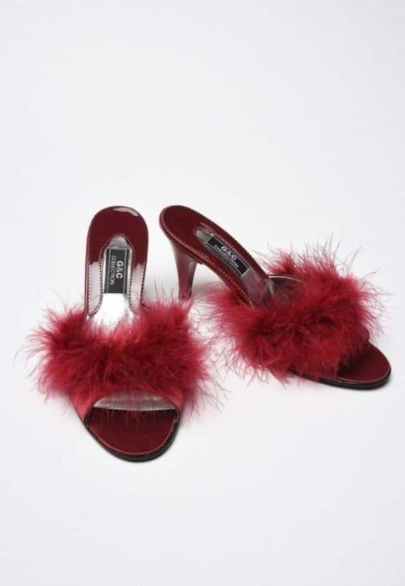 May include: A pair of red satin heeled slippers with fluffy feather trim. The slippers have a clear heel and the brand name "G&C Collection" is printed on the insole.