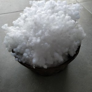 May include: A white, fluffy, polyester fiberfill in a brown basket. The fiberfill is used for stuffing pillows, cushions, and other home decor items.