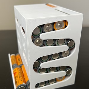 May include: White 3D printed battery organizer with multiple slots for AA batteries. The organizer is filled with AA batteries, some with orange tops and some with gray tops.
