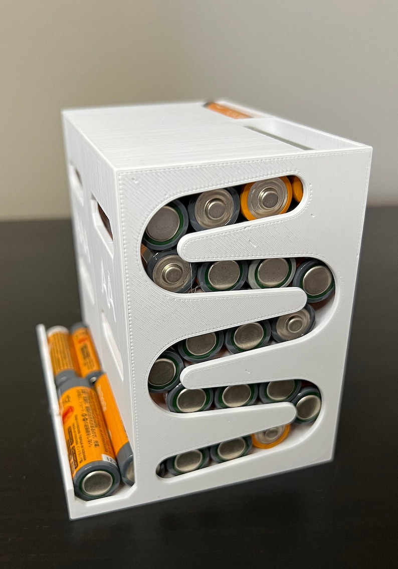 May include: White 3D printed battery organizer with multiple slots for AA batteries. The organizer is filled with AA batteries, some with orange tops and some with gray tops.