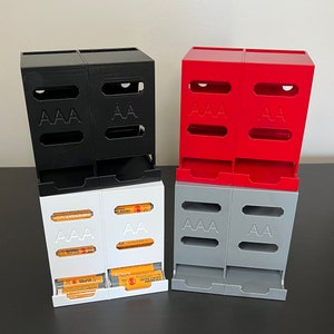 May include: Three sets of battery organizers, each with two compartments. The first set is black, the second is red, and the third is gray. Each compartment is labeled with "AAA" or "AA".