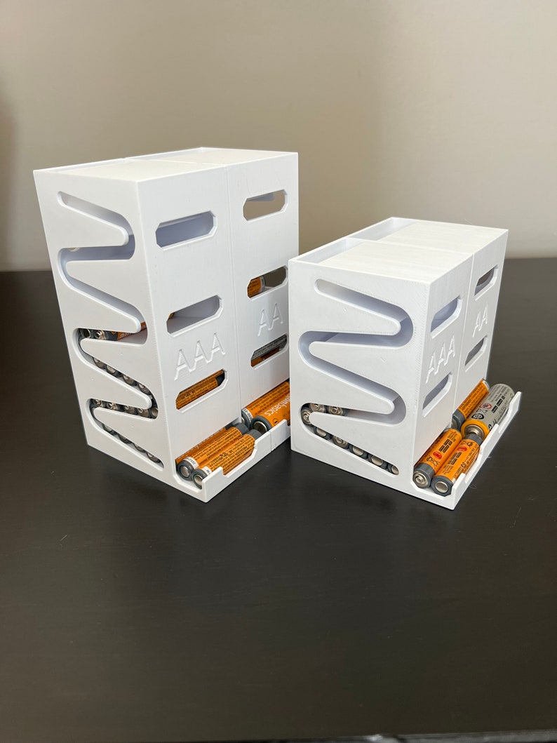 May include: Two white plastic battery organizers with slots for AAA batteries. The larger organizer has a row of batteries in the front slot.