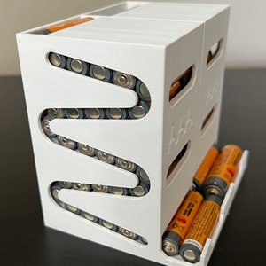 May include: White plastic battery organizer with a zig-zag design to hold AA batteries. The organizer has a separate compartment for AAA batteries.