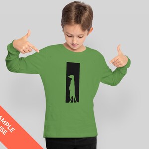Może przedstawiać: Zielony T-shirt z długim rękawem z czarną sylwetką surykatki stojącej w drzwiach.