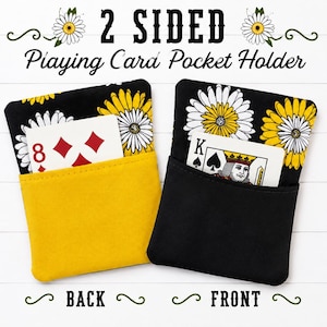 May include: Two fabric playing card pocket holders featuring a black background with white and yellow daisy patterns. One holder has a solid yellow front pocket containing an eight of diamonds card, and the other has a solid black front pocket containing a king of spades card. Text reads 2 SIDED Playing Card Pocket Holder, BACK, and FRONT.