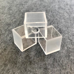 Puede incluir: Tres cubos de plástico transparente apilados uno encima del otro. El cubo superior tiene un pequeño agujero en el centro.