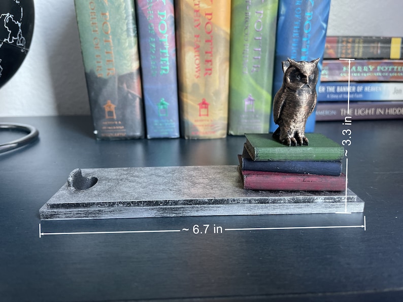 K&ouml;nnte beinhalten: Ein grauer Holzbuchst&uuml;tze mit einem Herz-Ausschnitt. Der Buchst&uuml;tze ist 17 cm lang und h&auml;lt einen Stapel von vier B&uuml;chern. Eine bronzene Eulenfigur sitzt auf den B&uuml;chern. Die B&uuml;cher sind 8,4 cm hoch.