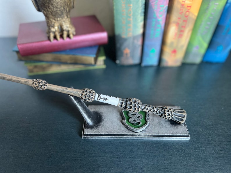 May include: A brown and black wand with a white inscription and a green and black crest on a grey stand.