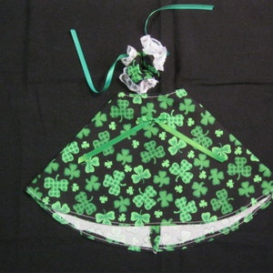 May include: A black and green shamrock print fabric skirt with white lace trim. The skirt has a green ribbon tied around the waist.