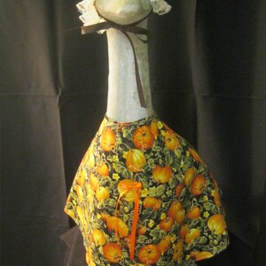 May include: A white ceramic goose figurine wearing a white lace bonnet and a black and orange pumpkin print dress with an orange ribbon.