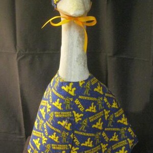 May include: A white goose wearing a blue and yellow fabric hat and a blue and yellow fabric dress with the words "West Virginia University" and "Mountaineers" printed on it.