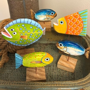 May include: Five hand-painted wooden fish figurines mounted on small square wooden bases with thin metal rods. The fish feature vibrant colors including lime green, bright orange, and shades of blue, with detailed scales, fins, and eyes.