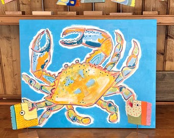 May include: A vibrant painting of a crab in shades of yellow, orange, and blue against a light blue background. The crab is the focal point, with detailed claws and body. Decorative fish sculptures are displayed above the painting, adding a whimsical touch.