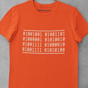 May include: Orange t-shirt with a white graphic of binary code. The code reads: 01001001 01001110 01000001 01010001 01001111 01000010 01001111 01010100