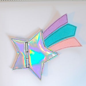 May include: A silver iridescent star with a pink, teal, and purple felt shooting star tail. The star is about 2 inches wide.