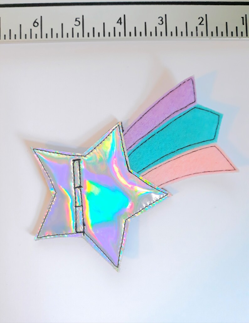 May include: A silver iridescent star with a pink, teal, and purple felt shooting star tail. The star is about 2 inches wide.