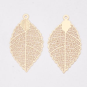 May include: Two gold leaf-shaped metal charms with intricate cut-out designs. The charms have a hole at the top for attaching to jewellery or other crafts.