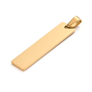 May include: A gold-coloured rectangular pendant with a loop at the top for a chain. The pendant has a smooth, polished surface and a simple, elegant design. The pendant is likely made of metal.