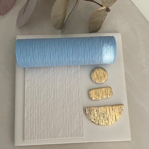 May include: A white ceramic tile with a blue textured roller, a gold textured circle, a gold textured rectangle, and a gold textured half-circle.
