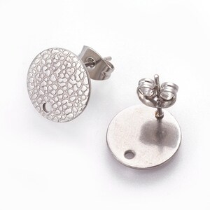 May include: Two silver-toned round earring blanks with a textured surface and a small hole in the centre. The earring blanks are designed for crafting and personalisation.