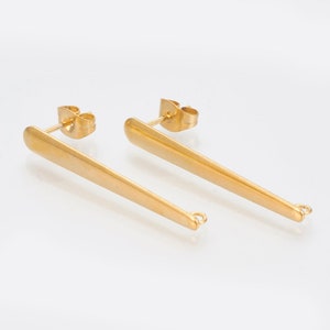 May include: A pair of gold-tone earrings with a long, thin, pointed design. The earrings have a post back closure and a small loop at the end.