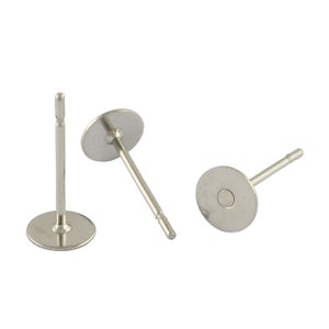 Op de afbeelding: Drie zilverkleurige oorbelpennen van dichtbij. Elke pen heeft een platte, ronde schijf en een rechte pen voor het inbrengen. De pennen zijn gemaakt van een glanzend, metalen materiaal.