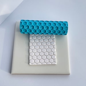May include: A blue and white silicone rolling pin with a honeycomb pattern. The rolling pin is on top of a white silicone mat with the same pattern.