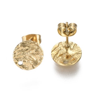 May include: A pair of gold-toned stud earrings with a textured circular design. The earrings have a post and butterfly backing.