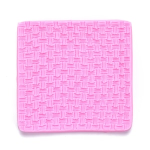 May include: Pink silicone baking mat with a woven pattern. The mat is designed to create a textured surface on baked goods.
