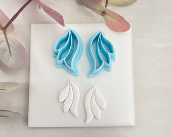Könnte beinhalten: Zwei blaue, plastikförmige Blätter-Ausstecher und zwei weiße Fondantblätter auf einer weißen Oberfläche.