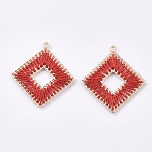 May include: A pair of gold-tone earrings with a square shape. The earrings are decorated with red thread that is woven into a square pattern.