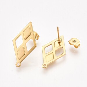 May include: A pair of gold-tone diamond-shaped earrings with a square cutout design. The earrings have a post back closure.