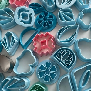 Puede incluir: Una colección de cortadores de galletas de plástico azul, rosa y verde en varias formas, incluyendo flores, hojas y diseños geométricos.