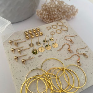 May include: A collection of gold-toned earring findings and hoops. The set includes earring posts, earring wires, and hoops of various sizes.