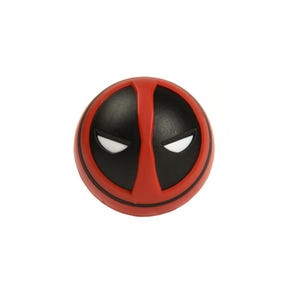 Pode incluir: Um objeto redondo vermelho e preto com o design da máscara do Deadpool. A máscara tem um fundo vermelho com áreas pretas para os olhos e a boca, e detalhes brancos para os olhos. O item é de cor sólida e tem uma superfície lisa.