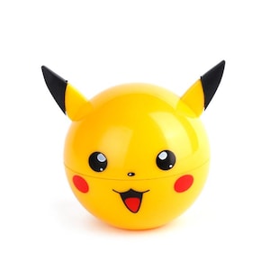 May include: A yellow Pikachu-shaped container with black-tipped ears, black eyes, red cheeks, and a smiling mouth. The container is round and has a glossy finish, resembling a character from the Pokémon franchise.