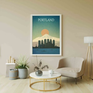 May include: A framed print of a city skyline with a mountain in the background. The print is in a white frame and has the word "PORTLAND" printed at the top. The skyline is in shades of blue and grey, and the mountain is in shades of brown and white. The sun is setting behind the mountain, and the sky is a gradient of blue and orange.