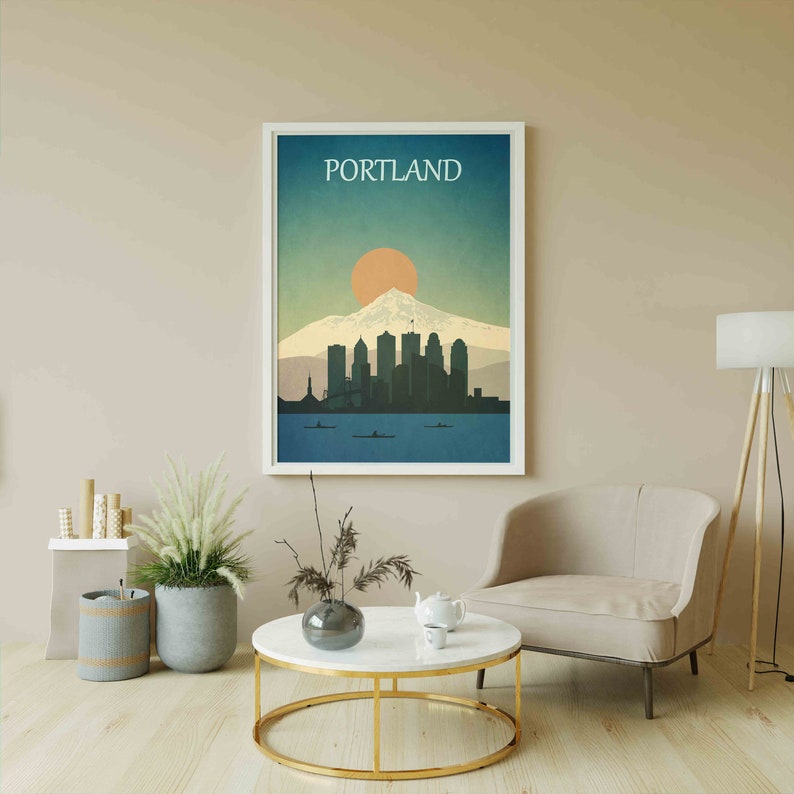 May include: A framed print of a city skyline with a mountain in the background. The print is in a white frame and has the word "PORTLAND" printed at the top. The skyline is in shades of blue and grey, and the mountain is in shades of brown and white. The sun is setting behind the mountain, and the sky is a gradient of blue and orange.