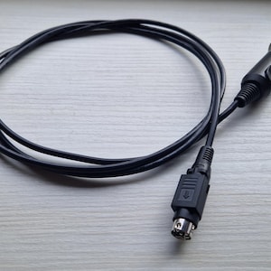 Puede incluir: Un cable de cargador de coche negro con un enchufe de encendedor de cigarrillos en un extremo y un conector en el otro extremo.