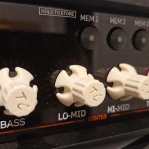 May include: Close-up of a black amplifier with white knobs labeled "Bass", "Lo-Mid", "Hi-Mid", "Treble", and "Tube Tone". The amplifier has a digital display and buttons labeled "Hold to Store", "Mem 1", "Mem 2", and "Mem 3".